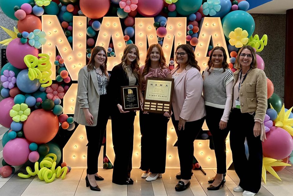 Group of students with plaques in front of NAMA sign.